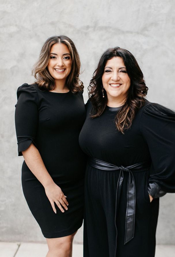 Two women in black dresses are standing next to each other and smiling.