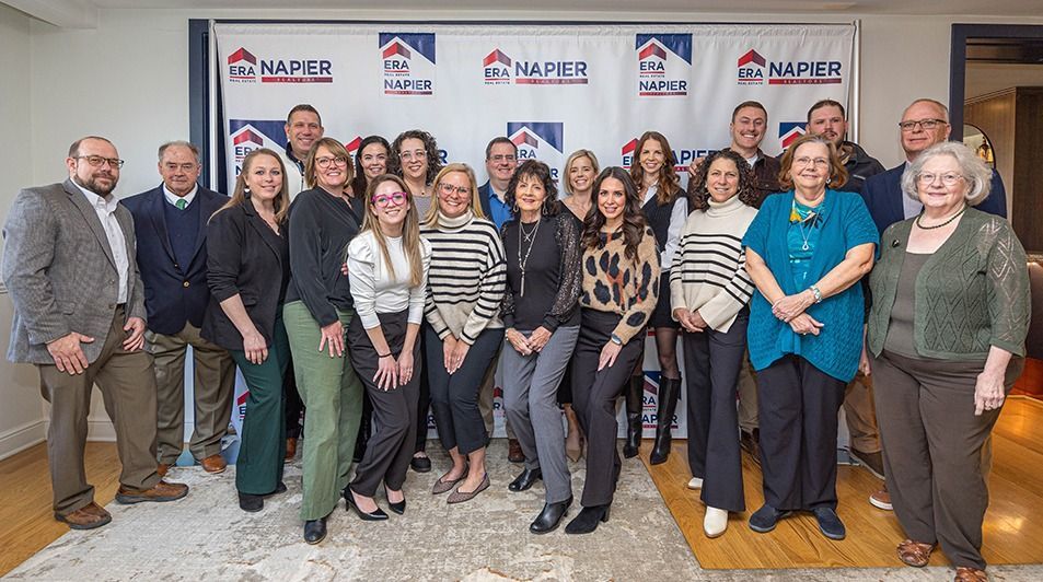 Group of people in front of a banner with a real estate logo, posed for a photo.