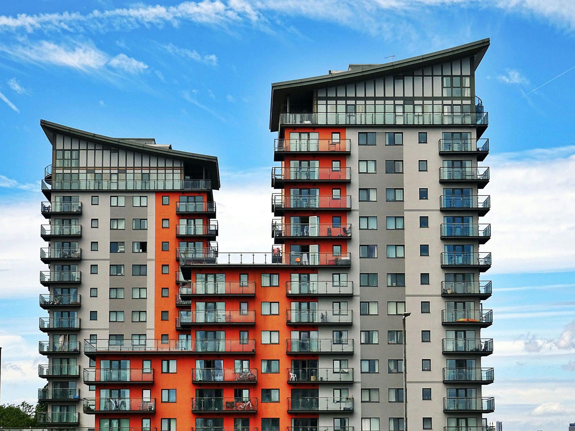 Two modern apartment buildings with orange and gray facades against a blue sky.