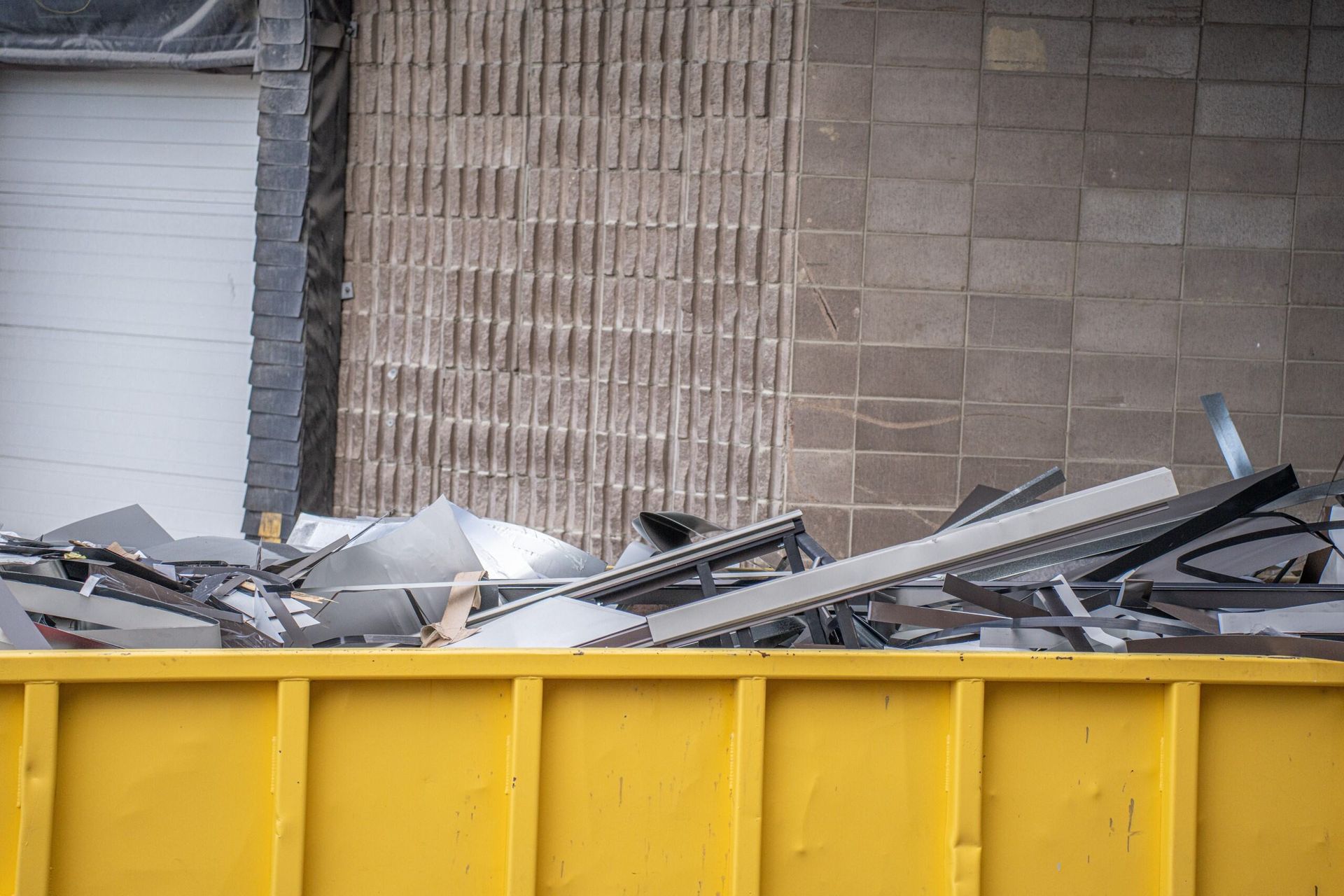 A Yellow Dumpster Filled With Scrap Metal in Front of a Building — Beehive Property Maintenance in Dysart, QLD