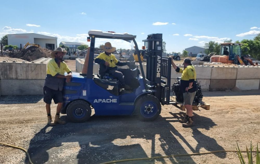 A Man in an Orange Shirt is Raking Gravel in a Yard — Beehive Property Maintenance in Emerald, QLD