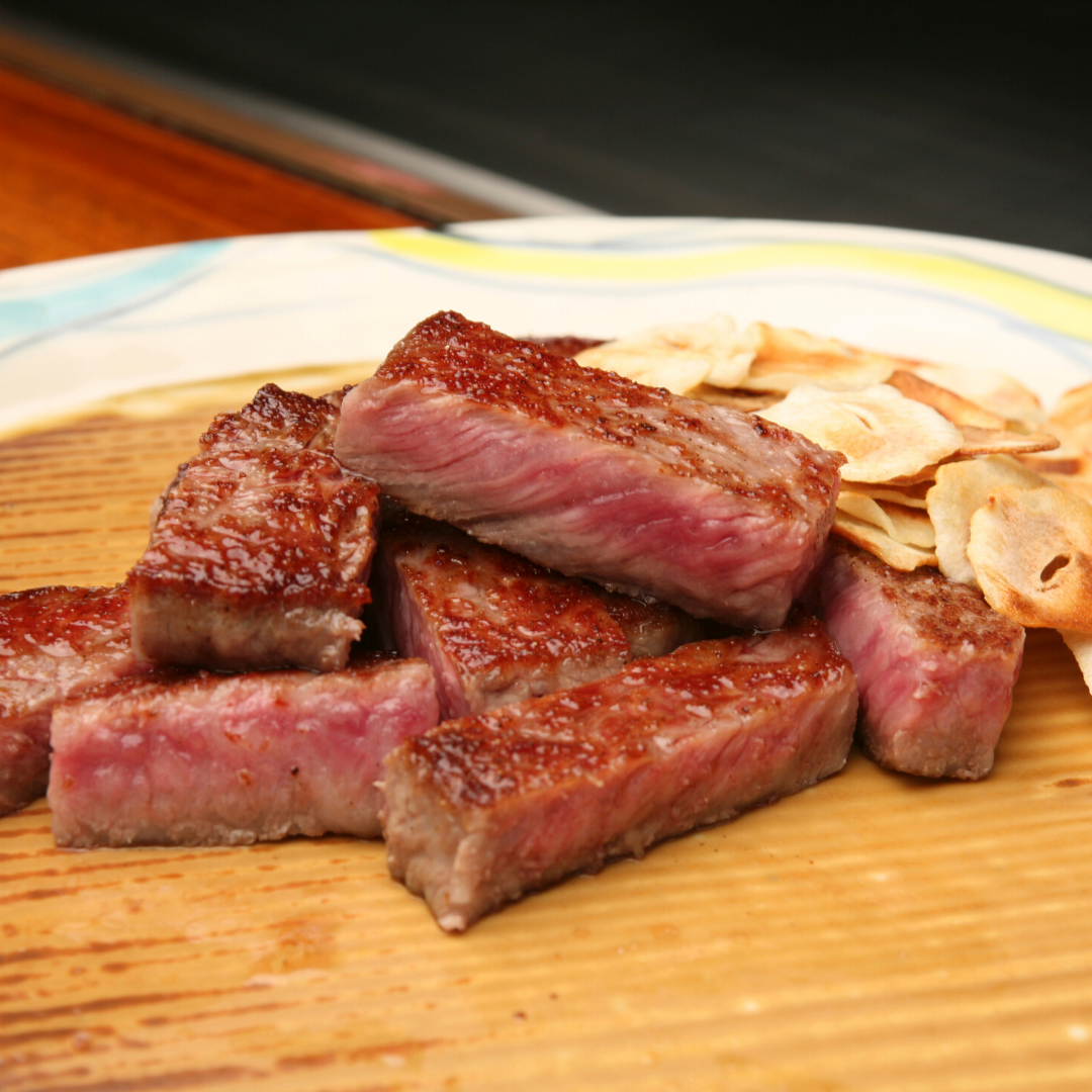 A wooden cutting board topped with steak and garlic chips