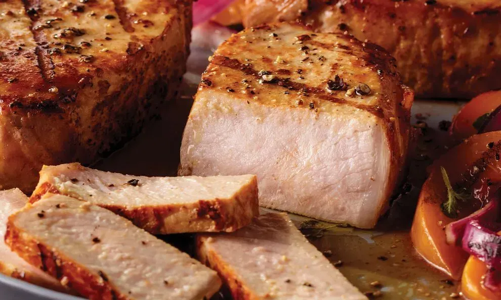 A close up of sliced pork chops on a plate with vegetables.