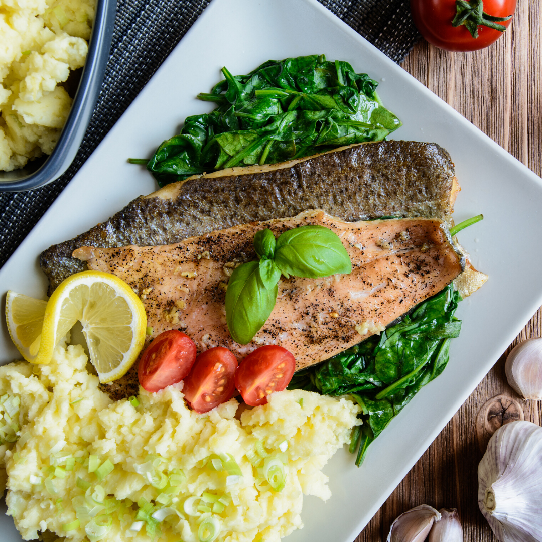 A white plate topped with fish , mashed potatoes , tomatoes and spinach.