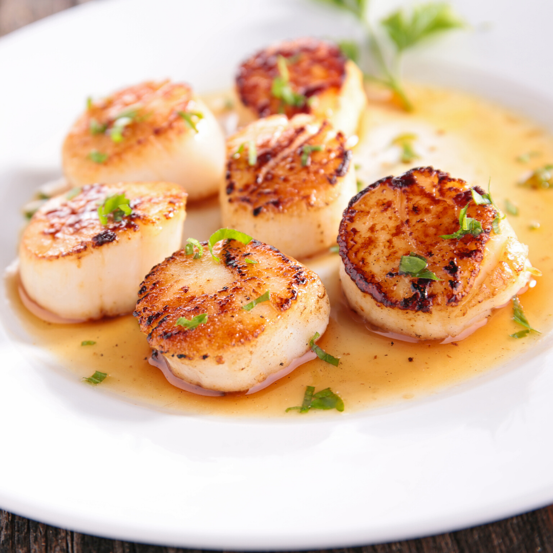 A white plate topped with scallops and sauce on a wooden table.