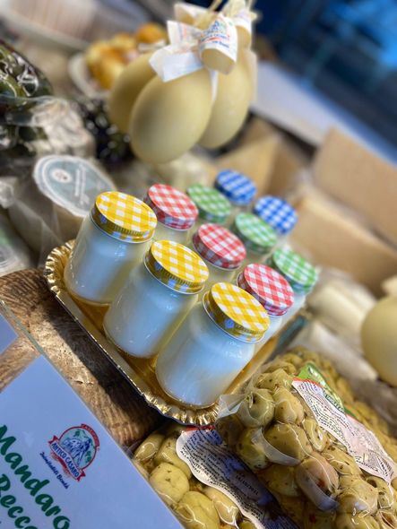 Vetrina con prodotti caseari: barattoli, formaggi e olive. Coperchi ed etichette colorati, colori vivaci.