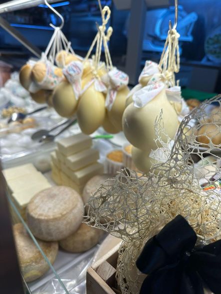 Esposizione di formaggi: varie forme, tra cui sfere dorate appese, quadrati impilati e forme rotonde.