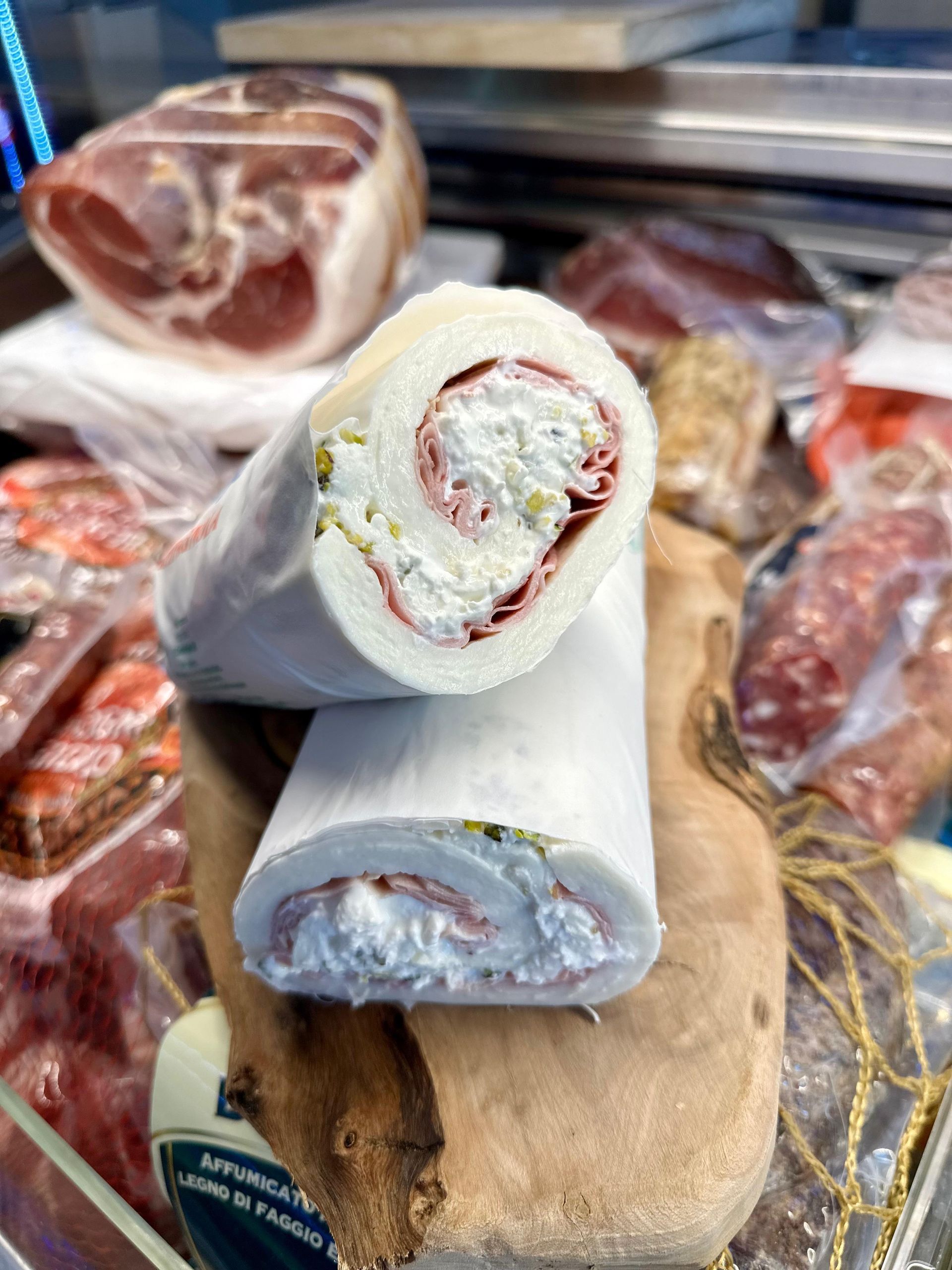 Due rotoli di formaggio bianco e fette di prosciutto con ripieno cremoso, su un tagliere di legno, vetrina per la carne.