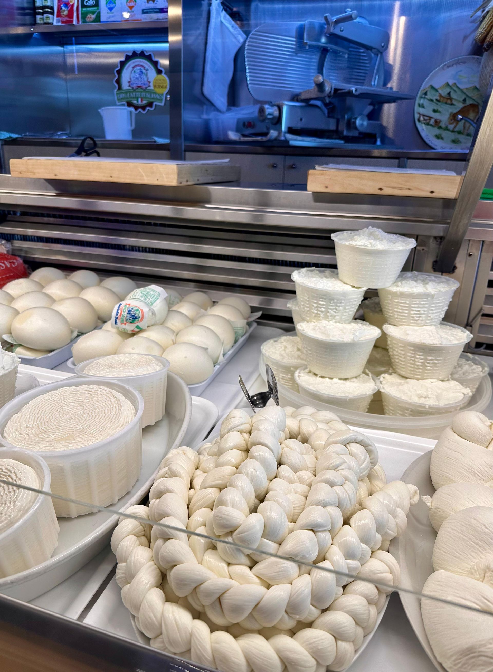 Formaggi esposti in un mercato: varietà intrecciate, a palla e a tazza.