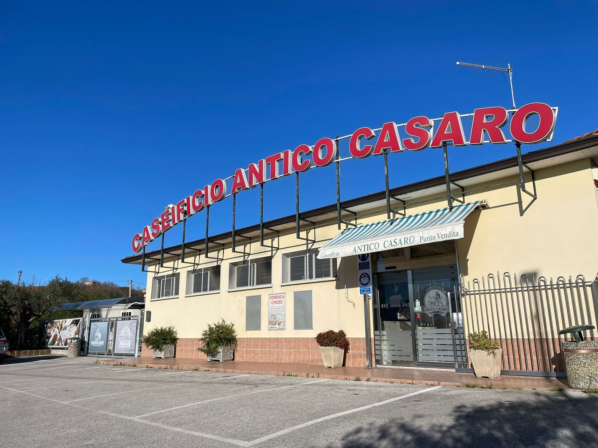 "Negozio Casaro Antico con insegna rossa, edificio beige, sfondo cielo azzurro."