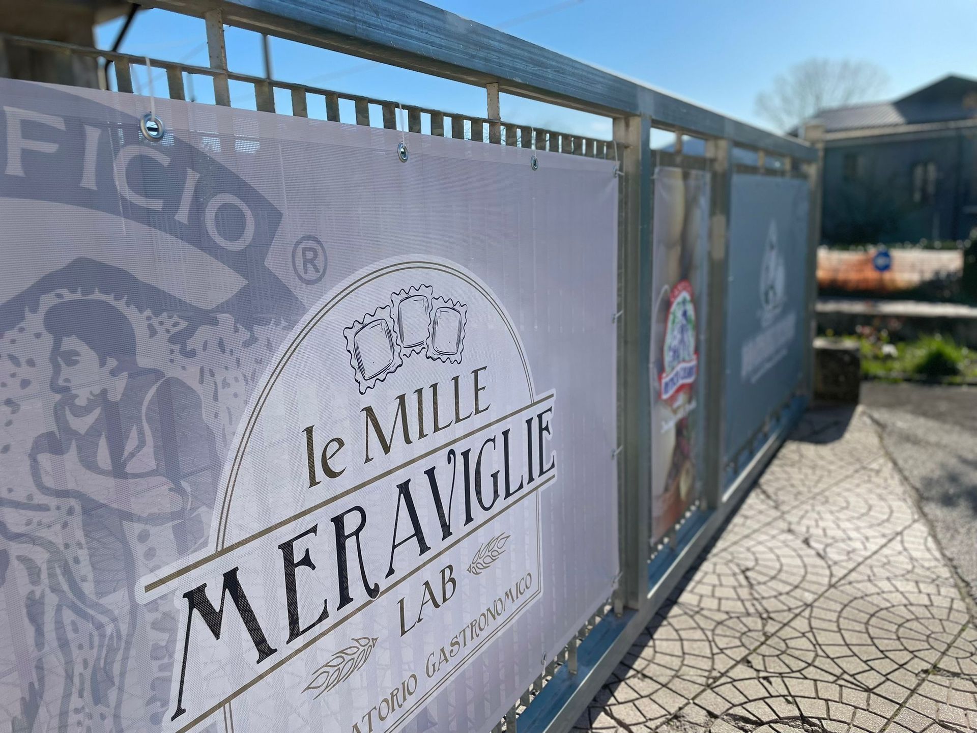 Struttura in metallo con striscione pubblicitario "Le Mille Meraviglie Lab" davanti a un edificio.