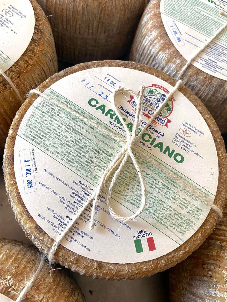 Diversi formaggi a forma di pera, in un cesto e appesi, con noci, una bottiglia e dettagli in legno.