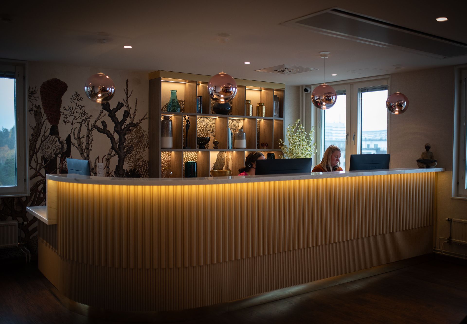 Reception Tandläkargruppen Täby C med bakgrundsbelyst träfasad, en person som sitter bakom och dekorativa föremål på hyllor.