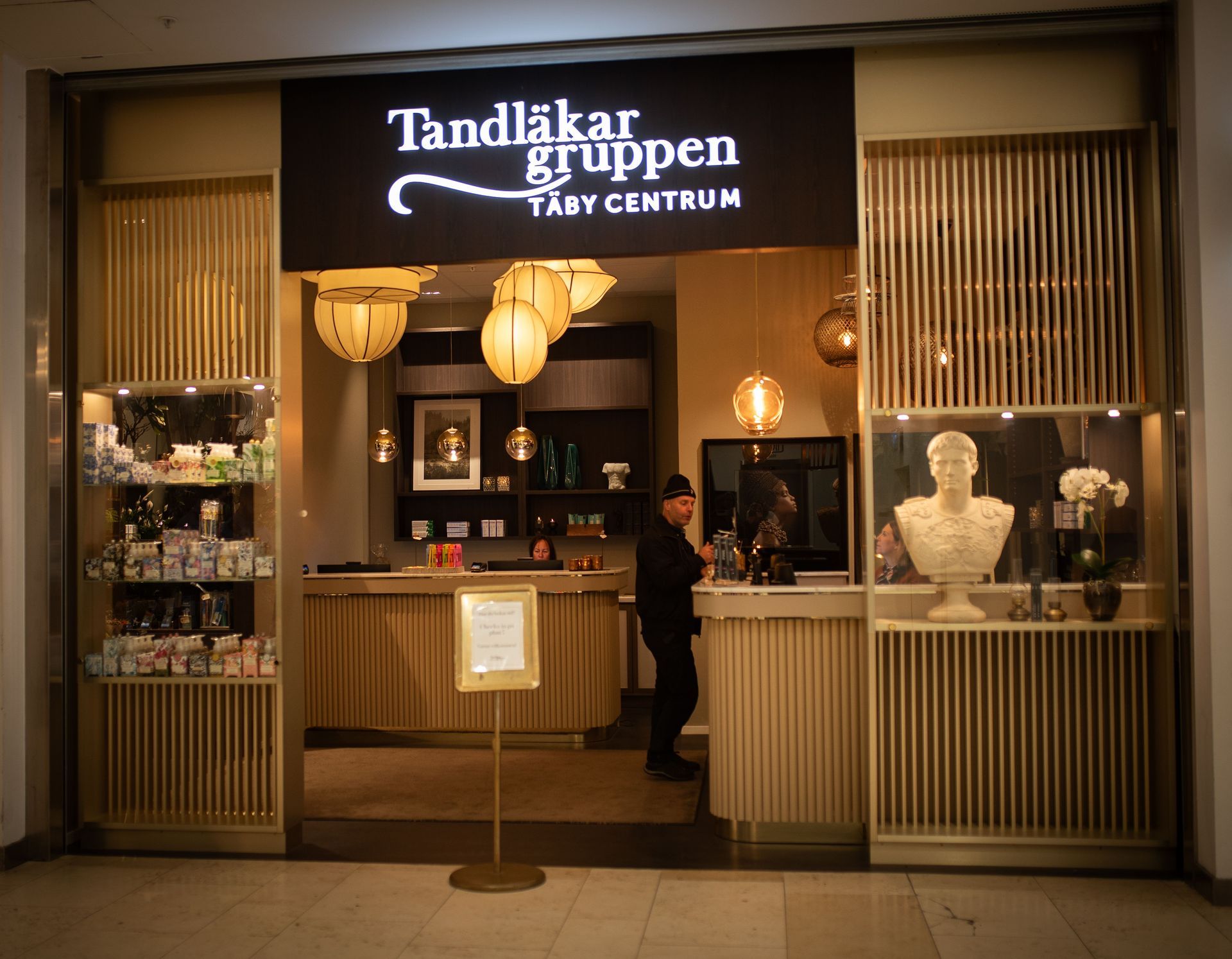 Entrén till Tandläkargruppen, en tandklinik i Täby Centrum, Sverige. Fasaden har trädetaljer, hängande lyktor och en byst.