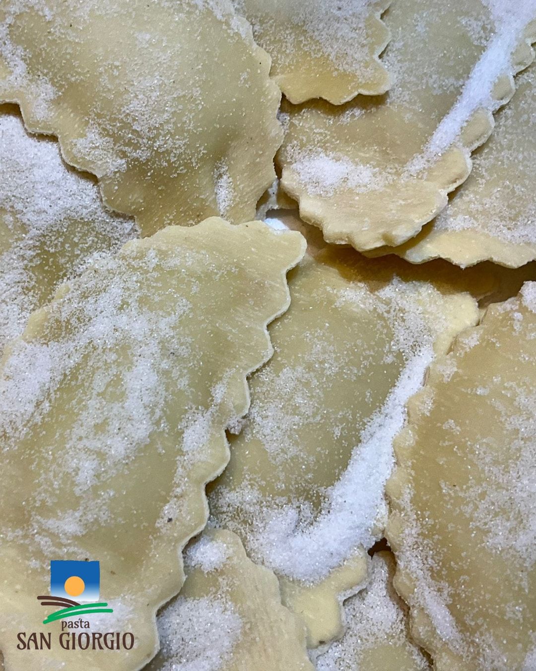 Primo piano di ravioli freschi infarinati; logo Santa Giorgio in un angolo.