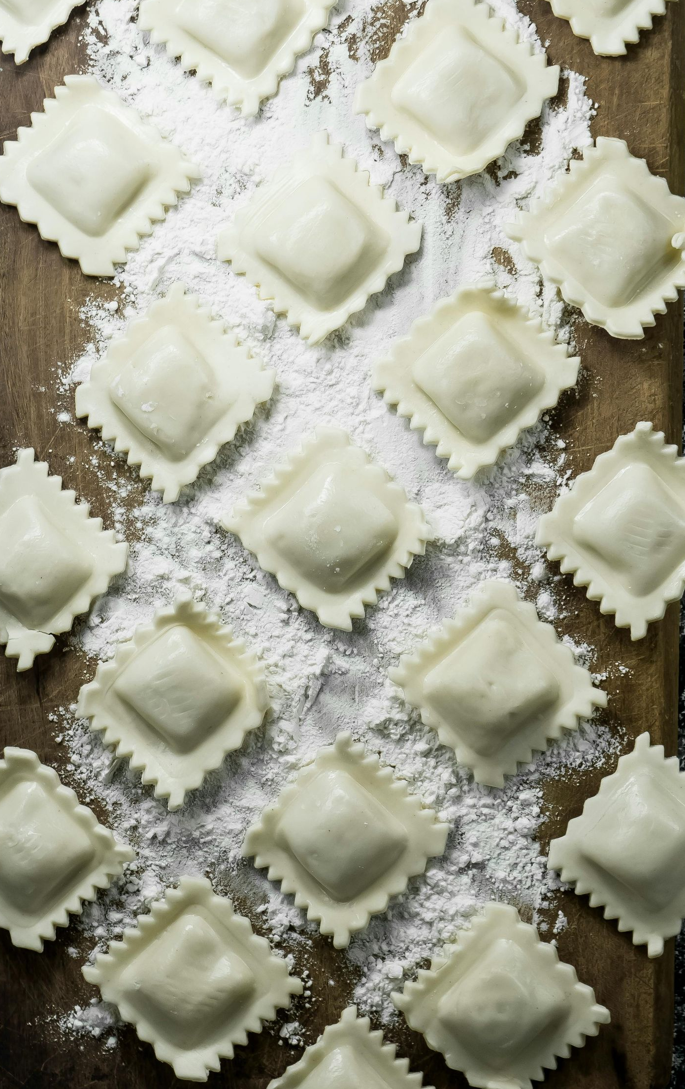 Quadrati di ravioli infarinati e disposti su una superficie di legno.