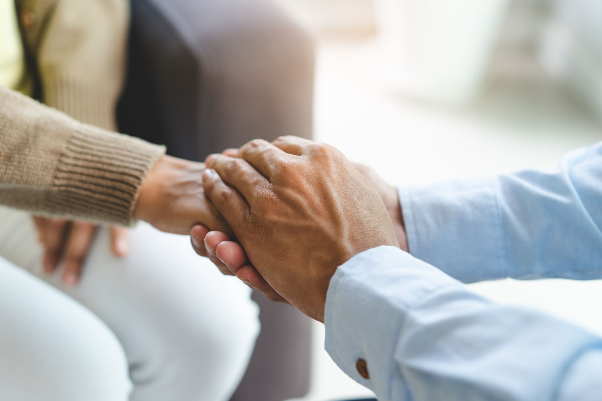 A man and a woman are holding hands while sitting on a couch.