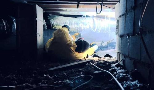Two workers in yellow protective suits crawl in a crawl space, near insulation and concrete blocks. Two workers in yellow protective suits crawl in a crawl space, near insulation and concrete blocks.