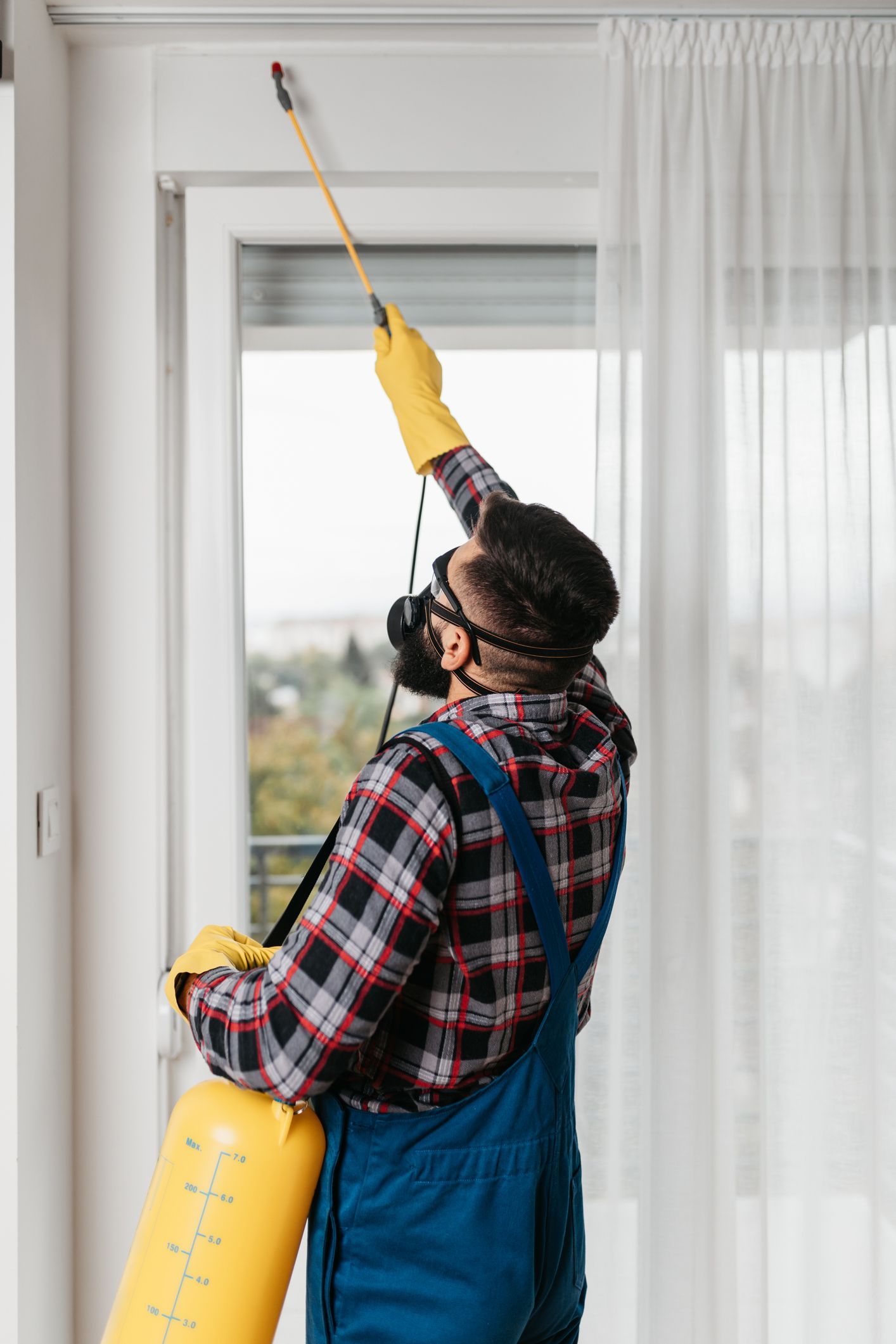 Man in protective gear spraying pesticide near a window. Man in protective gear spraying pesticide near a window.