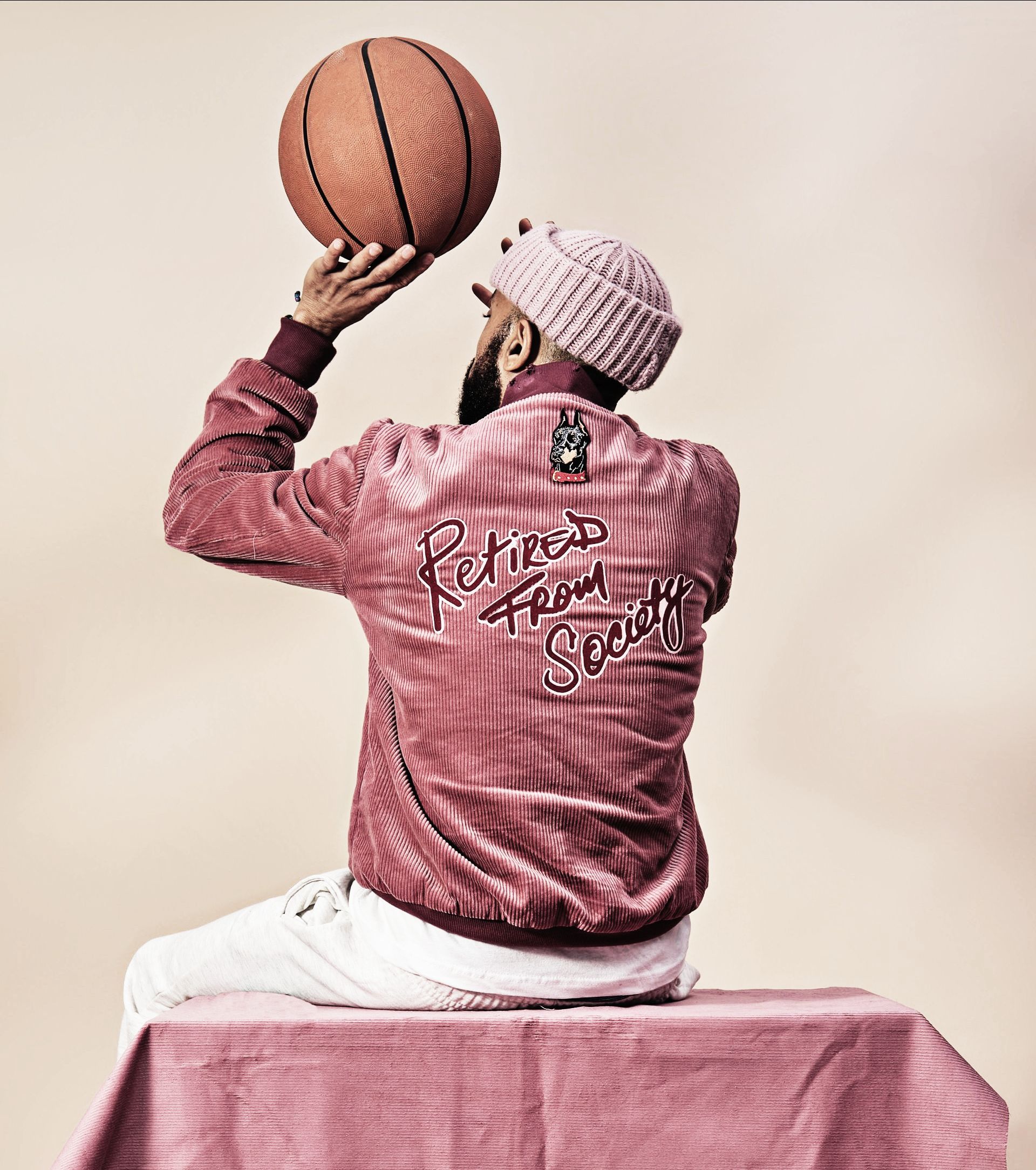 Person in pink jacket and hat, seated, about to shoot basketball.