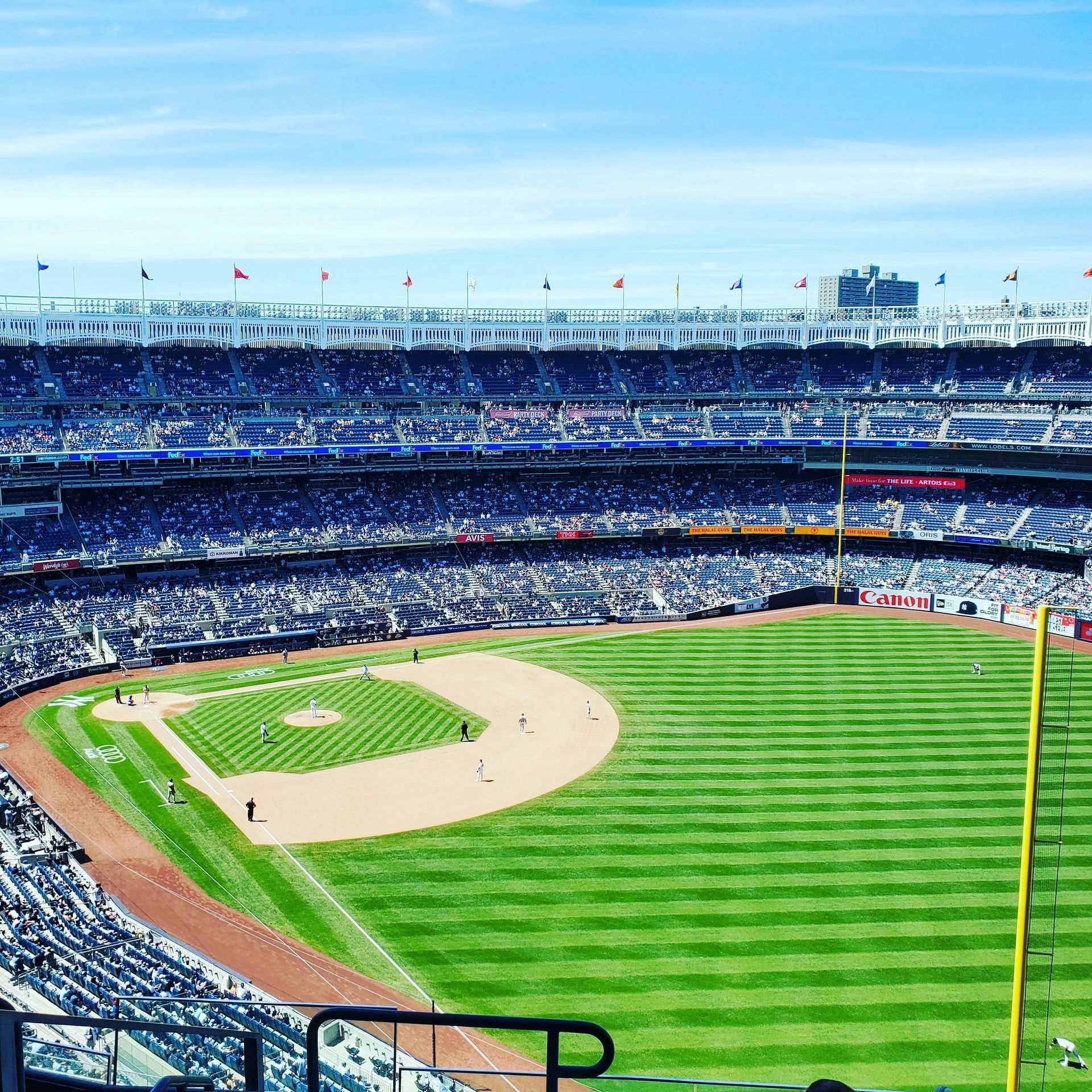 Baseball stadium filled with fans, green field, blue sky.