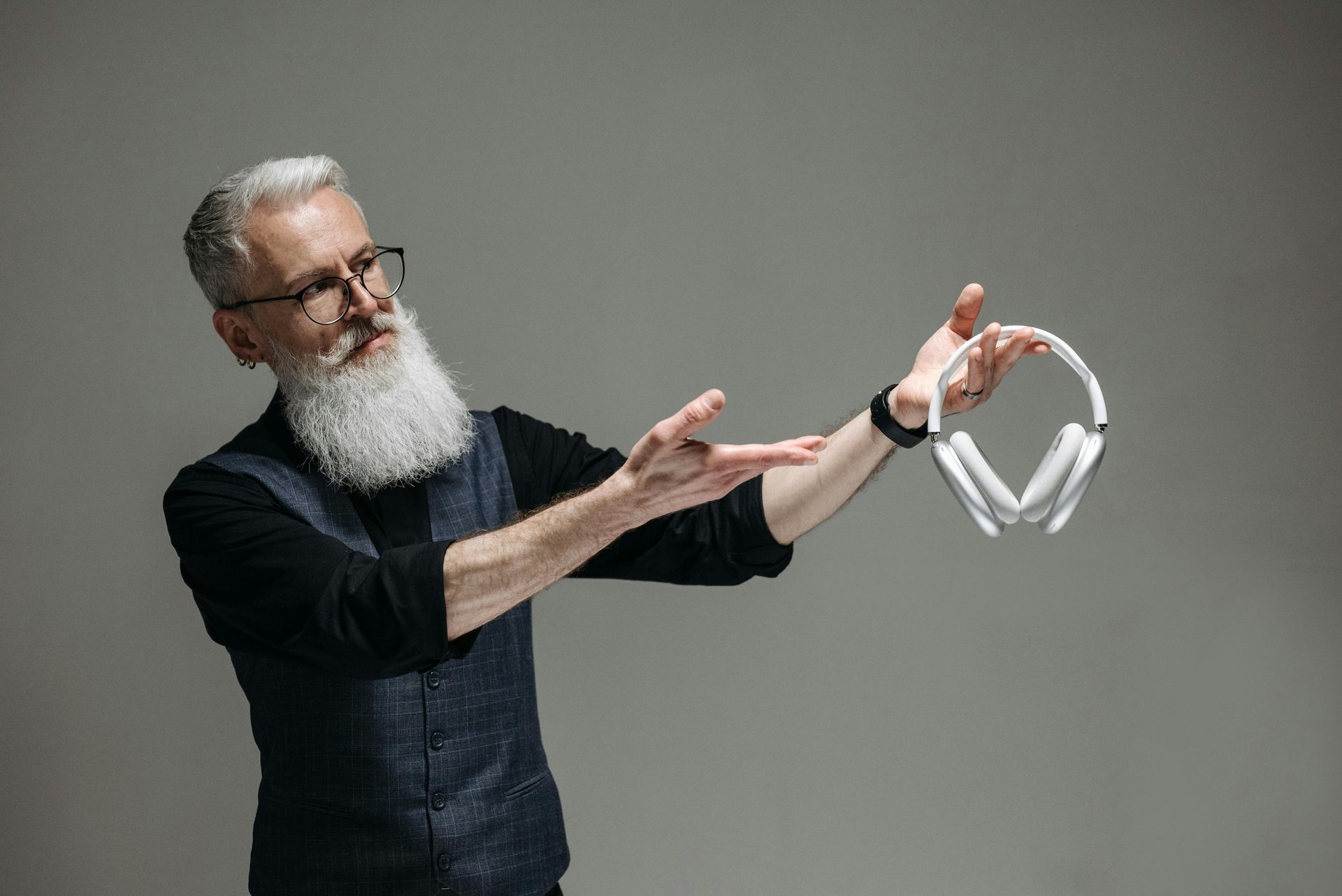 Man with gray beard and glasses levitates white headphones in front of a gray background.