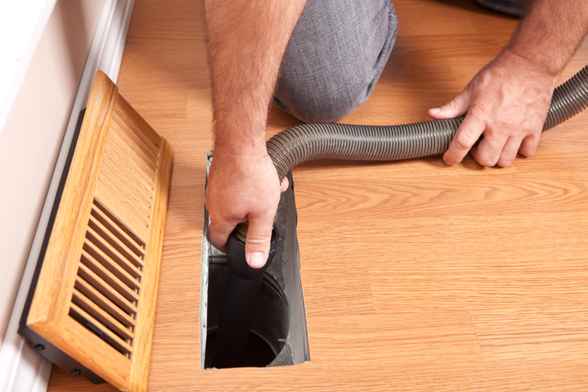 A man is using a vacuum cleaner to clean an air vent.