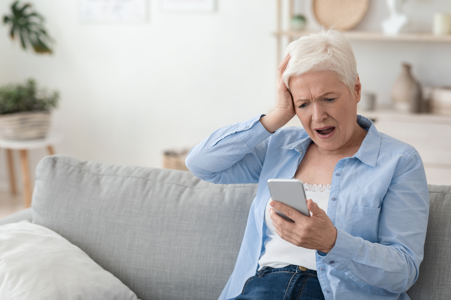 An elderly woman is sitting on a couch looking at her cell phone.