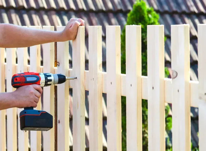 A man is using a drill to install a wooden fence.
