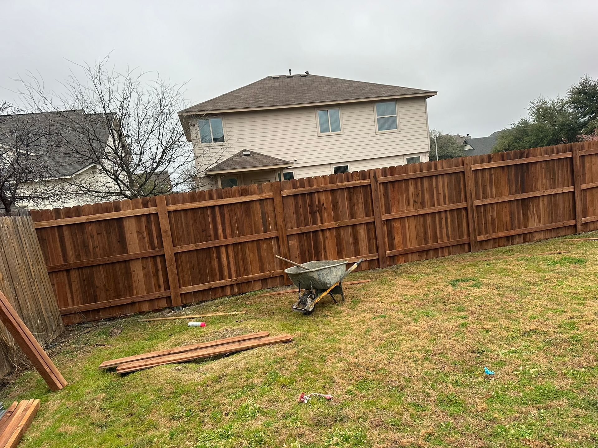 A wooden fence is being built in a backyard with a wheelbarrow in the foreground.