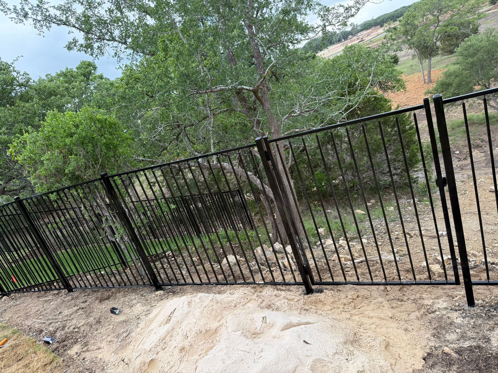 A black wrought iron fence surrounds a dirt field with trees in the background.