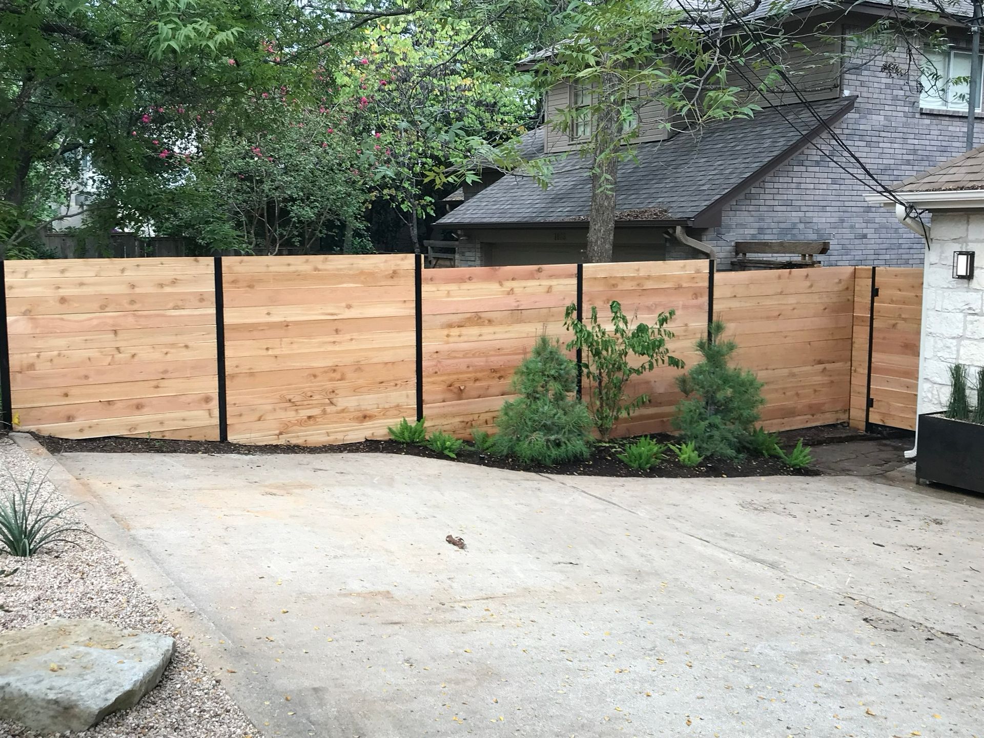 A wooden fence is surrounding a driveway in front of a house.