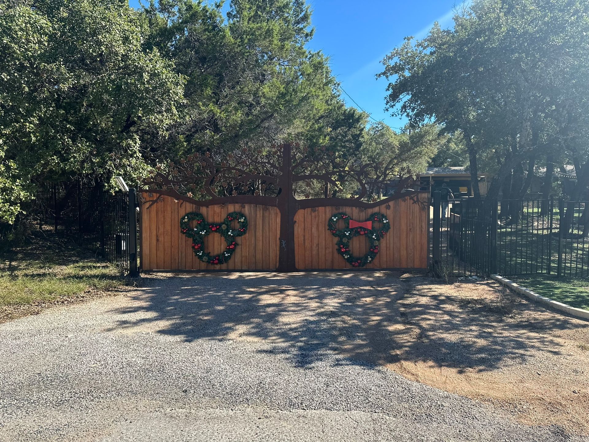 A wooden gate with mickey mouse wreaths on it is surrounded by trees.