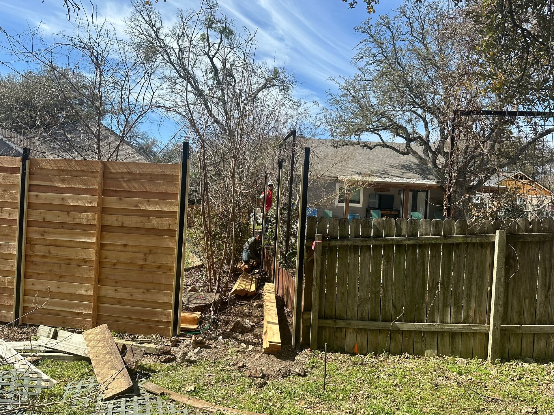 A wooden fence is being built in the backyard of a house.