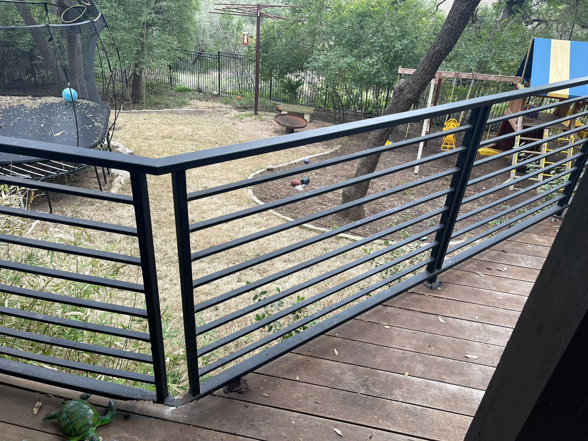 A black railing on a wooden deck with a view of a park.