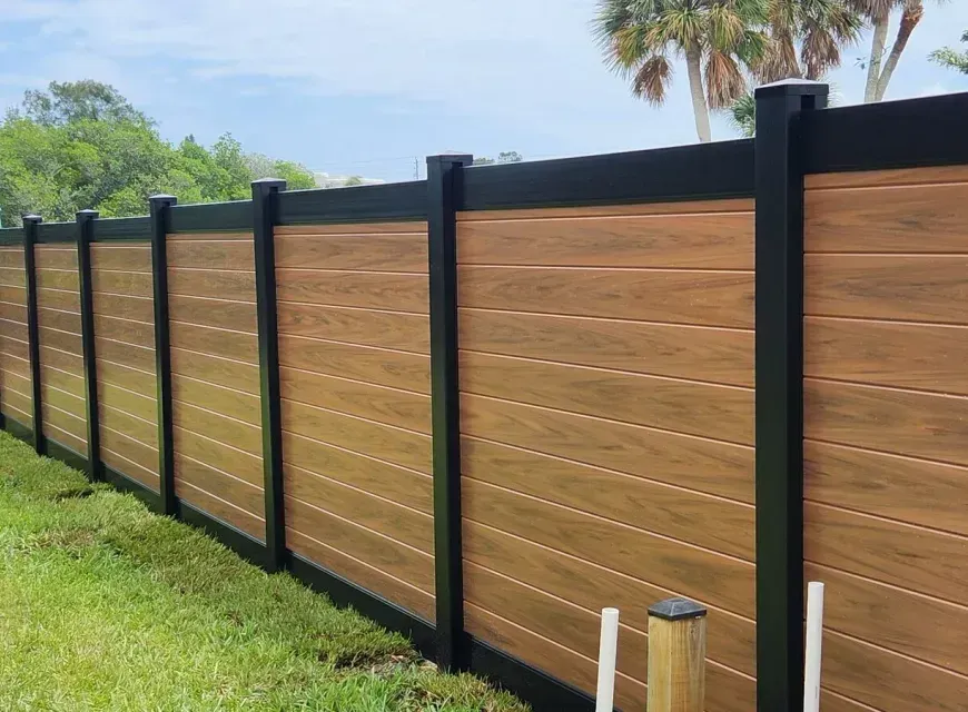 A wooden fence with black posts is sitting on top of a lush green field.