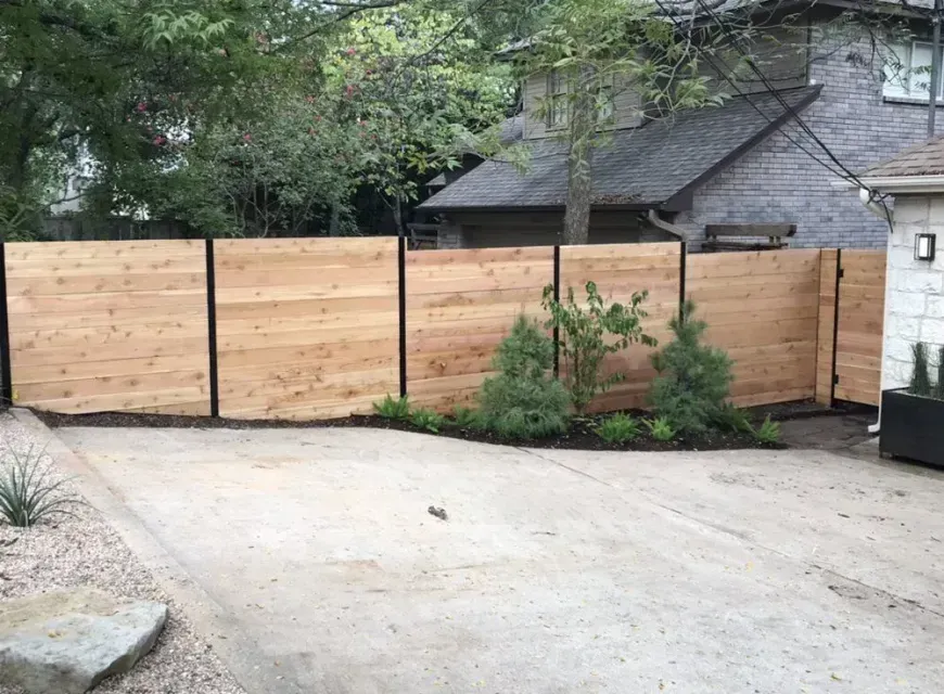 A wooden fence surrounds a driveway in front of a house.