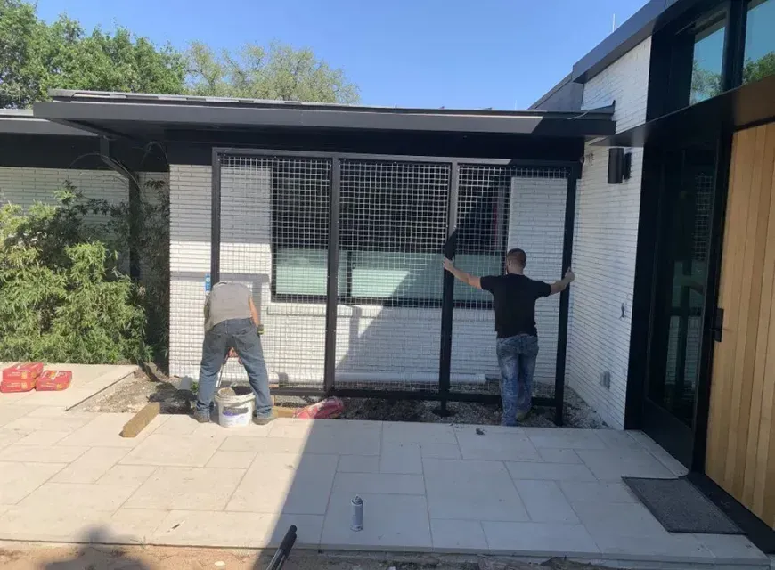 Two men are working on a fence in front of a house.