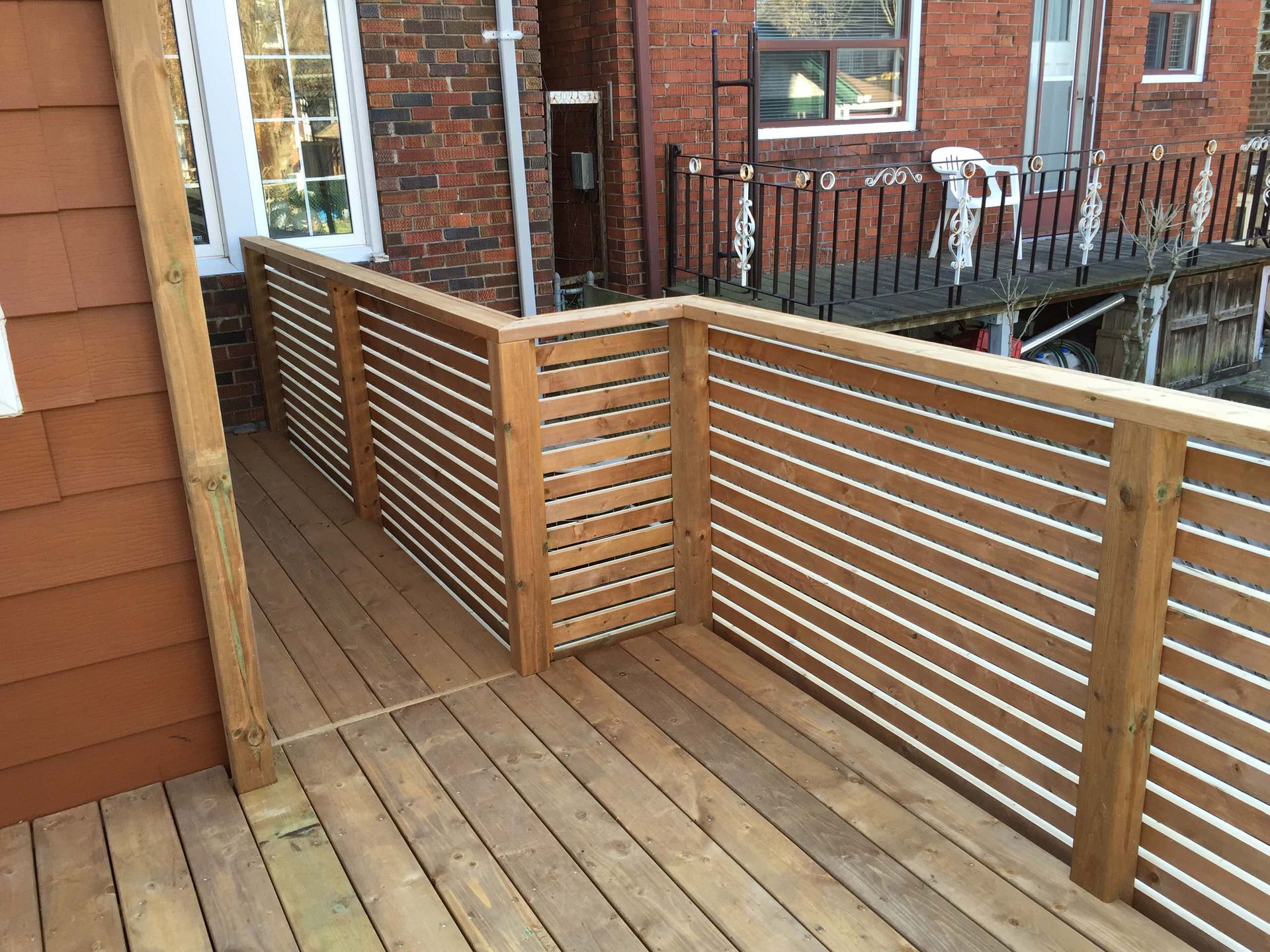A wooden deck with a metal railing and a brick building in the background.