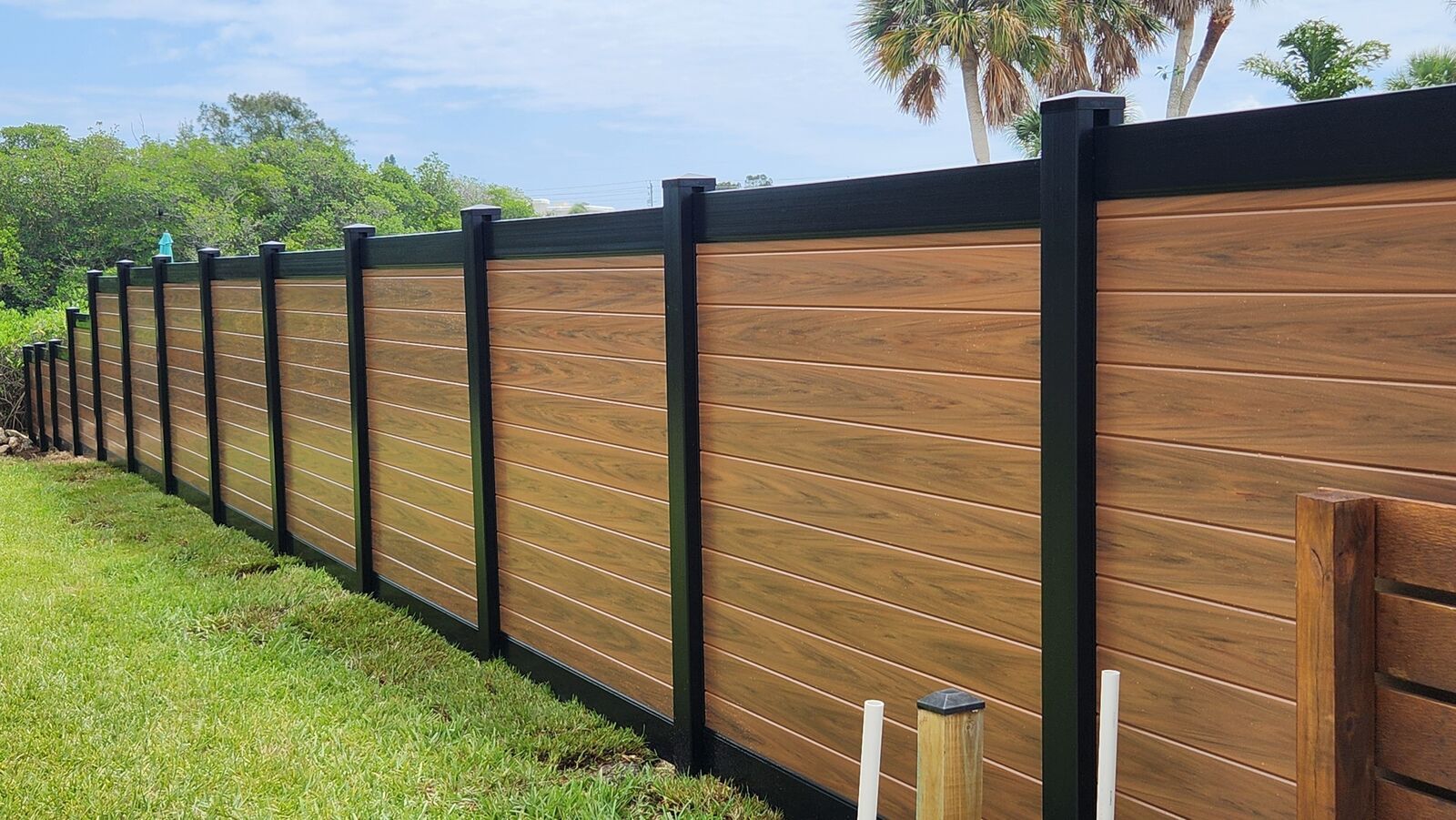 A wooden fence with black posts is sitting on top of a lush green field.