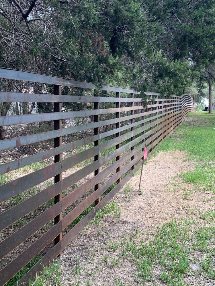 A wooden fence surrounds a grassy field with trees in the background.