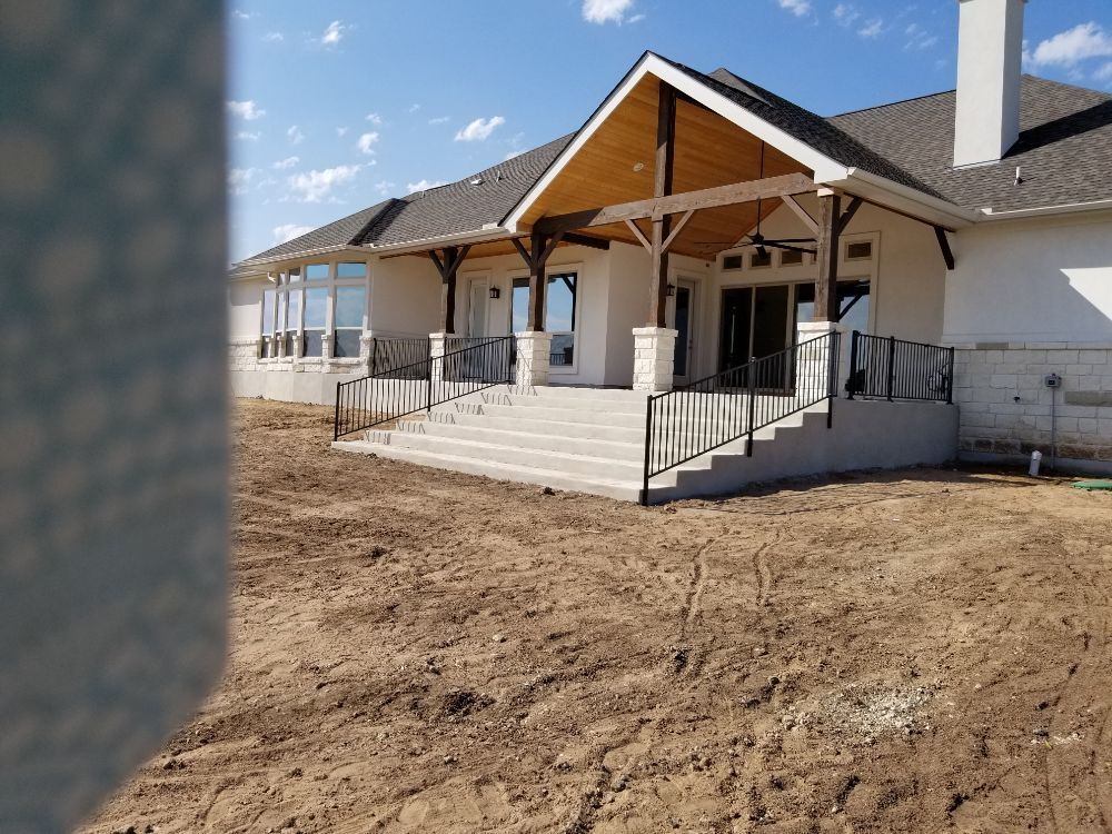 A large white house with a porch and stairs is sitting on top of a dirt field.