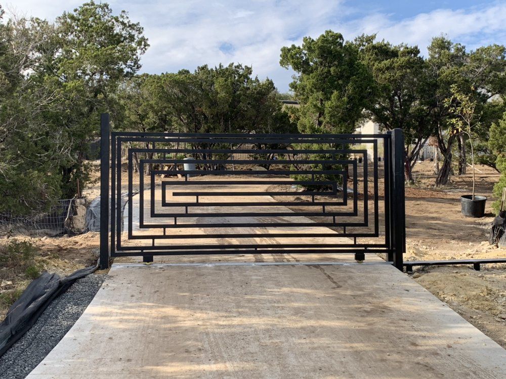 A black gate with a maze design is surrounded by trees.
