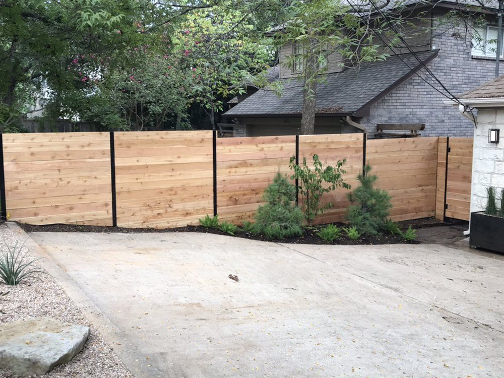 A wooden fence surrounds a driveway in front of a house.