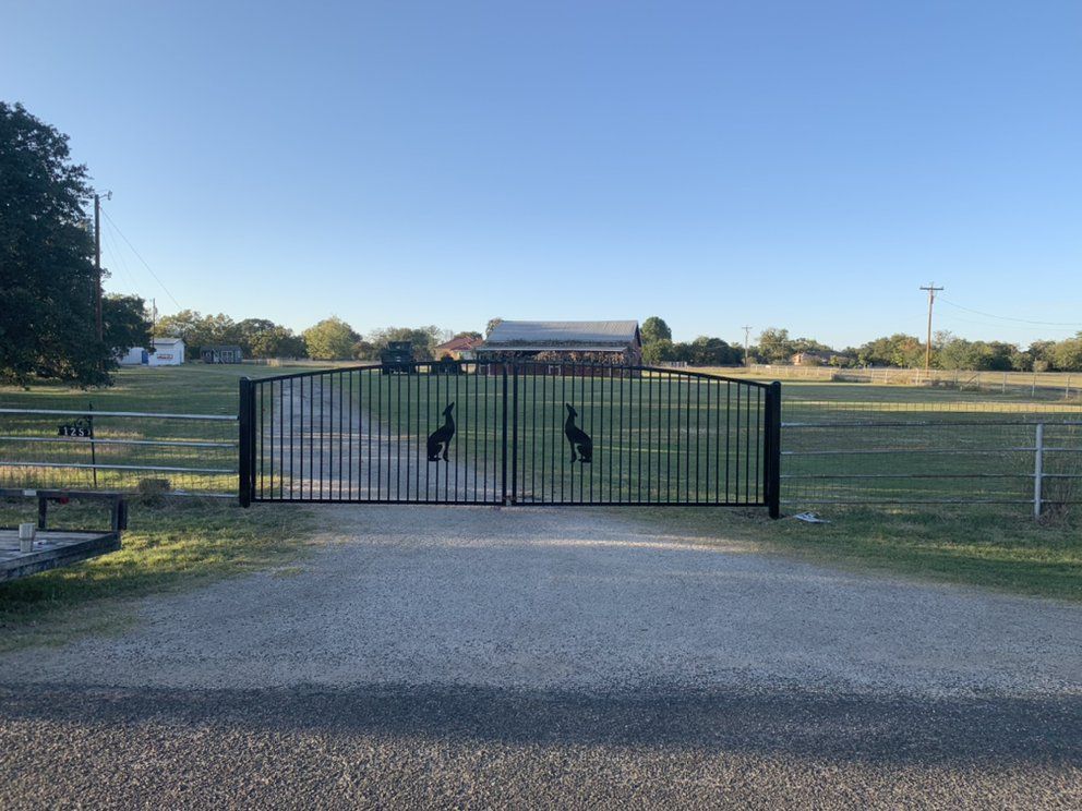 A metal gate with a picture of a turkey on it is surrounded by a dirt road.
