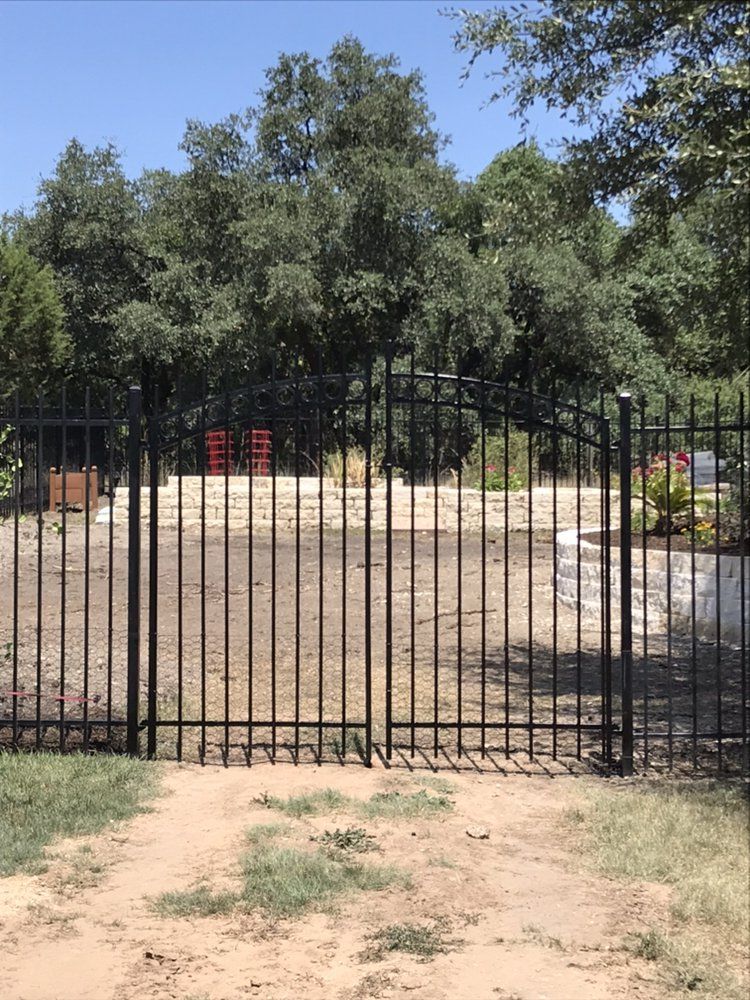 A black wrought iron fence surrounds a dirt field with trees in the background.