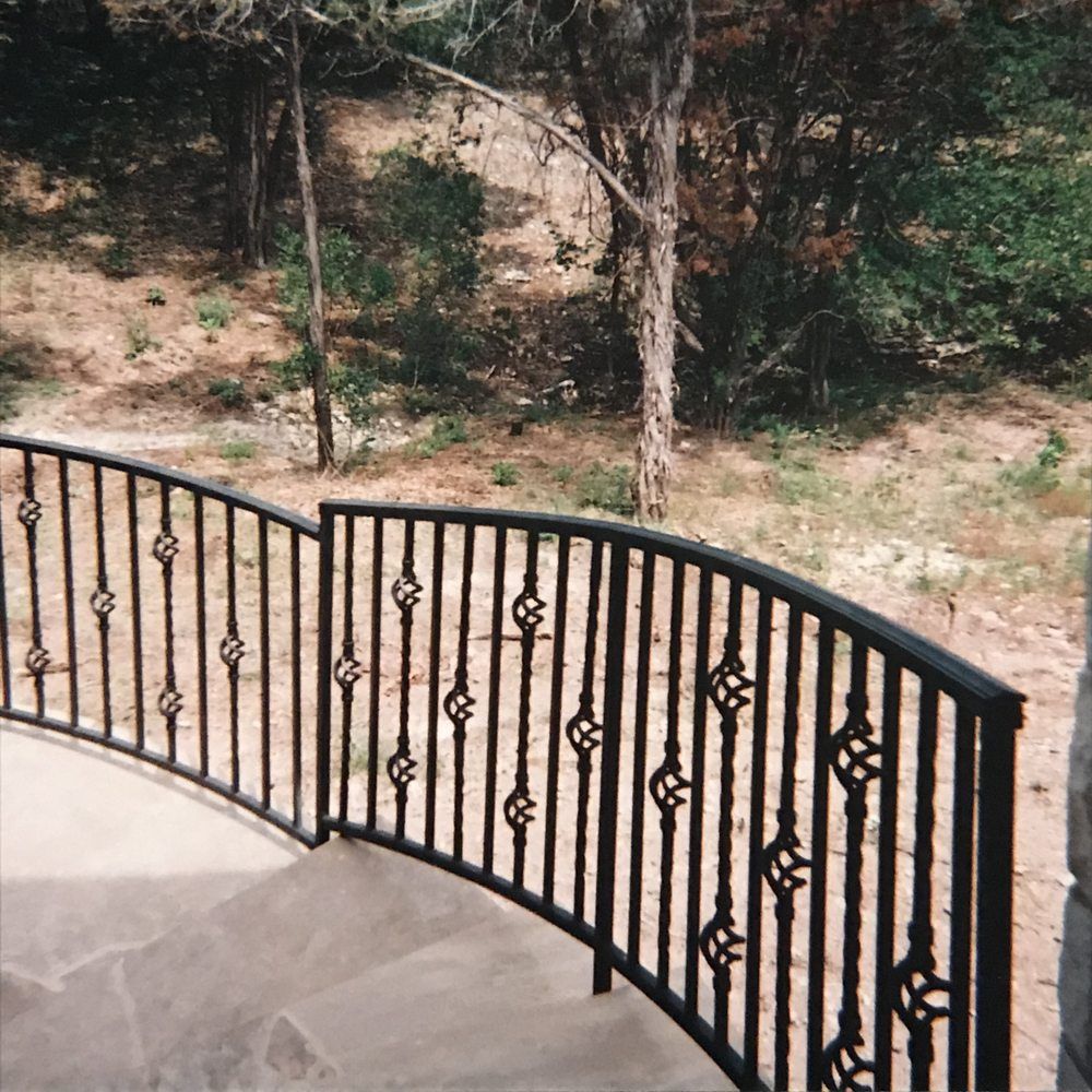 A wrought iron railing on a balcony with trees in the background