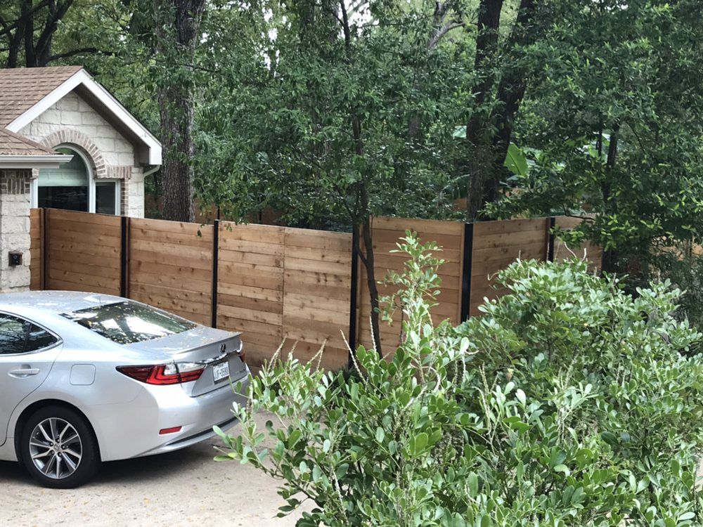 A silver car is parked in front of a wooden fence.