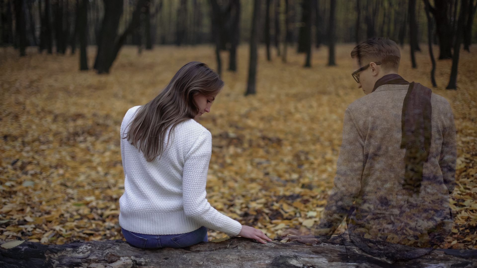 A man and a woman are sitting on a rock in the woods.