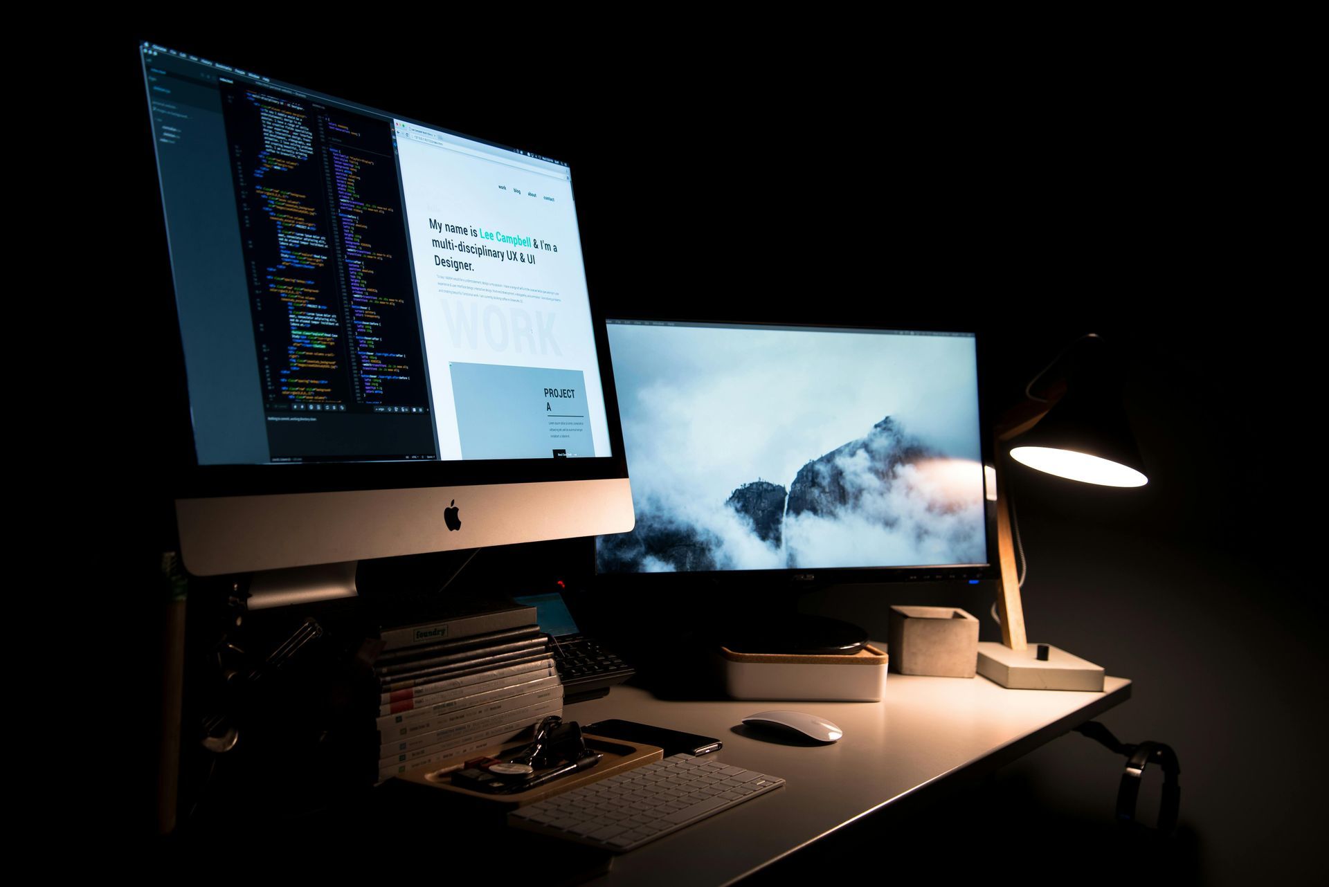 Two computer monitors are sitting on a desk in a dark room.